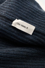 Nahaufnahme aus schräger Perspektive des Lisa Yang Cashmere Schals 'Marseille' graublau, voluminös mit markanter Rippstruktur und Label.