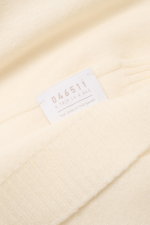 Nahaufnahme des cremefarbenen 04651/ A trip in a bag Cashmere Schals mit weichem Griff, Rippstrickkanten und Logo-Label, frontal fotografiert.