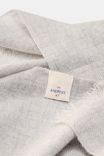 Close-up top-down view of andrea's 1947 Cashmere scarf light grey melange showing pure cashmere fabric, very soft touch, fine lightweight quality, narrow fringed edge, and tag; dimensions approx. 198 cm x 62 cm.