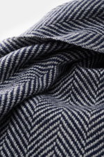 Close-up from a slightly above angle of the Brunello Cucinelli Cashmere scarf grey/dark blue patterned, showing a two-tone woven fabric with a classic herringbone pattern and narrow fringed edge. 

<p>Quiet-luxury label BRUNELLO CUCINELLI is known for its