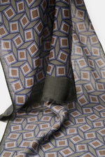 Close-up front view of the Altea Scarf grey green/smoky blue/brown patterned, hanging to show smooth texture, lightweight quality, rolled edges, narrow fringed hem, graphic print, mix of wool and modal, dimensions approx. 182 cm x 53 cm.