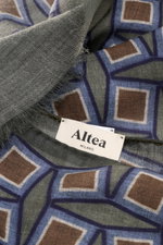 Close-up front view of the Altea Scarf grey green/smoky blue/brown patterned showing its graphic print, smooth texture, rolled edges, narrow fringed hem, made of a mix of wool and modal, lightweight quality, dimensions approx. 182 cm x 53 cm.