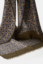 Altea Scarf dark brown/brown/grey blue patterned shown close-up from the side, featuring a graphic print, mix of wool and modal, smooth texture, lightweight quality, rolled edges, narrow fringed hem, dimensions approx. 182 cm x 53 cm.