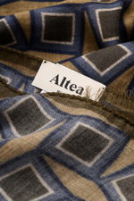 Close-up front view of the Altea Scarf dark brown/brown/grey blue patterned showing rolled edges, narrow fringed hem, smooth texture, lightweight mix of wool and modal, graphic print, dimensions approx. 182 cm x 53 cm.