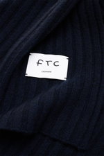 Close-up top view of the FTC Cashmere scarf navy showing wide rib knit pattern and large woven logo label.

Description:  
<p>An elegant, sustainably produced accessory for cold days: This scarf with rib knit pattern by FTC is made of luxurious, pure fair
