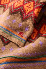 Nahaufnahme aus schräger Perspektive des Polo Ralph Lauren Schal hellbraun/rot/orange gemustert mit markantem Fair-Isle-Strickmuster, feinem Strickbild, dezenten RL-Initial-Stitching und doppellagiger, wärmender Qualität aus Wolle, Baumwolle und Leinen.