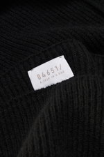 Nahaufnahme des schwarzen 04651/ A trip in a bag Cashmere Schals mit klassischem Patentstrickmuster und weißem Markenlabel, fotografiert aus schräger Perspektive.