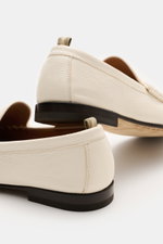 Close-up rear-side view of Officine Creative Penny Loafer 'Balfron' creme in supple deerskin with a slightly tapered silhouette, penny strap, decorative stitching on the toe cap, leather lining, and leather sole, highlighting its stylish and durable summe