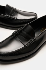 Church's Penny Loafer 'Rowley' schwarz aus poliertem Glattleder mit Ziernähten, Penny-Strap, schmal zulaufender Silhouette, ledernem Innenfutter, von oben fotografiert.