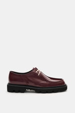 Side view of Collegium Derby 'Pillar Moc-Toe' bordeaux in polished smooth leather with narrow silhouette, two-hole lace, decorative toe stitch, leather lining, and black rubber lug sole, eyecatcher for transitional seasons.