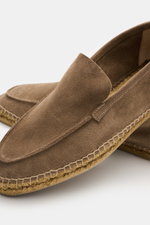 Close-up angled view of Castañer Espadrilles 'Nino T' taupe in supple suede with a slightly tapered cut, decorative toe seam, practical pull loop, braided jute edging, and flexible natural rubber sole, showcasing summery lightness and Mediterranean style 