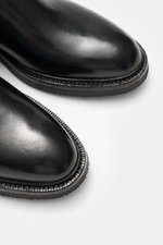 Close-up top-front view of the Officine Creative Chelsea Boot 'Dude Flexi' black in polished smooth leather with Goodyear welted frame, slightly tapered silhouette, side elastic inserts, practical pull tab, leather lining, and natural rubber outsole. Move