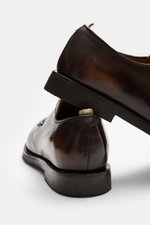 Close-up side and rear view of Officine Creative Sneaker 'Sequel' taupe, showcasing fine suede leather, rounded toe cap, side perforations, seven-hole lacing, padded collar, logo emboss on tongue, grosgrain pull tab, leather lining, and flexible rubber so