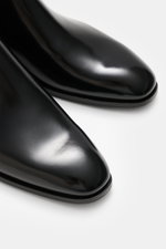 Santoni Chelsea Boot 'Adrian' black shown from a close-up front-side angle, featuring polished smooth leather, narrow tapered silhouette, side elastic inserts, practical pull tab, leather lining, and leather sole with rubber insert. With SANTONI, you are 