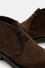 Nahaufnahme des Santoni Desert Boot 'Collin' dunkelbraun, leicht schmal zulaufend, aus geschmeidigem Veloursleder mit offener Zwei-Loch-Schnürung, ledernem Innenfutter und Kautschuk-Laufsohle, frontale Perspektive.