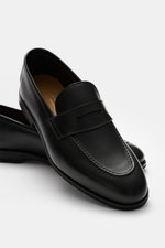 Close-up front-side view of the Henderson Penny Loafer 'Royal' black, made of finely grained leather with typical penny strap, narrow tapering silhouette, decorative toe cap stitching, Goodyear-welted construction, leather lining, rubber outsole, and heel