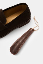 Close-up top-side view of the Henderson Penny Loafer 'Modica' dark brown made of supple suede leather with visible leather lining and natural rubber outsole, accompanied by a brown leather shoehorn with stitched edge.

Description:  
<p>Stylish classic: T