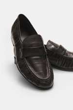 The Row Loafer dunkelbraun aus softem, exotischem Aal-Leder mit typischem Strap, Ziernaht und schmaler Silhouette, seitlich fotografiert.