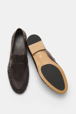 The Row Loafer dark brown in soft eel leather, photographed from above showing top and sole views, with typical strap, grained look, narrowing silhouette, decorative front seam, leather lining, leather sole, and rubber inserts for comfort.