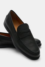 Tod's Penny Loafer schwarz aus geschmeidigem Leder, schmale Silhouette, typischer Penny Strap, Steppnaht auf der Vorderkappe, Gummisohle mit Noppen, seitliche Nahaufnahme.