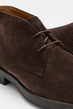 Nahaufnahme des dunkelbraunen Tod's Desert Boot aus edlem Veloursleder, seitliche Perspektive mit offener Zwei-Loch-Schnürung, schmal zulaufender Silhouette, praktischer Anziehschlaufe, Innenfutter aus Leder und leicht profilierter Gummisohle.