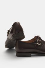 Crockett & Jones Monk 'Monkton' dark brown shoes in polished smooth leather, narrow tapering silhouette, buckle over instep, rubber outsole, stitched sole shown from rear and side angle.