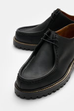 Close-up front-side view of Sebago Wallabee 'Dockside' black shoes in sturdy nubuck leather with round silhouette, two-eyelet lacing, decorative seam, leather lining, and rugged rubber sole with tread, practical for the transitional season.