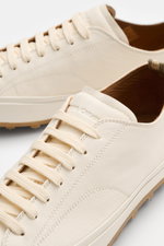 Close-up front-side perspective of Officine Creative Sneaker 'Vulcan' offwhite in finely grained leather with round toe, seven-hole lacing, logo-embossed tongue, leather lining, and studded rubber sole, showcasing a modern retro look perfect for office an