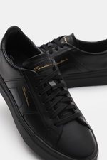 Santoni Sneaker 'Double Buckle' schwarz aus edlem Glattleder, sieben-Loch-Schnürung, runde Vorderkappe, tonale Overlays, seitlich mit Emblem, gepolsterter Schaftrand, Innenfutter aus Leder, flexible Kautschuksohle mit Schriftzug, frontal fotografiert.