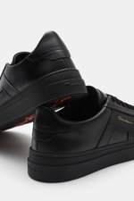 Santoni Sneaker 'Double Buckle' schwarz aus edlem Glattleder, seitlich mit goldfarbenem Emblem, flexible Kautschuksohle, Rückansicht schräg.
