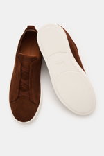 Zegna Slip-on-Sneaker 'Triple Stitch' braun shown from top and sole views, featuring soft suede, round toe, crossed elastic bands, padded collar, pull tab, embossed tongue, leather lining, and flexible rubber sole. <p>In Anlehnung an das ikonische Stitchi
