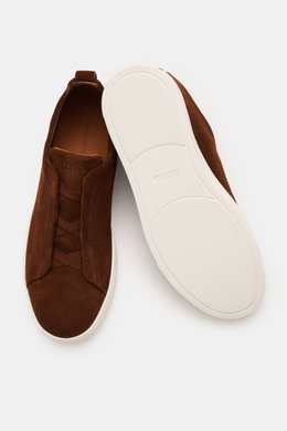 Zegna Slip-on-Sneaker 'Triple Stitch' braun shown from top and sole views, featuring soft suede, round toe, crossed elastic bands, padded collar, pull tab, embossed tongue, leather lining, and flexible rubber sole. <p>In Anlehnung an das ikonische Stitchi