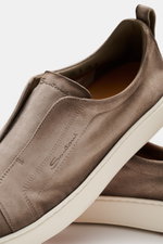 Santoni Slip-on-Sneaker 'Victory' taupe aus Veloursleder, schmal zulaufend, mit Gummizug-Lasche, Logoprägung, Anziehschlaufe, Lederfutter, Gummisohle, Nahaufnahme seitlich oben.