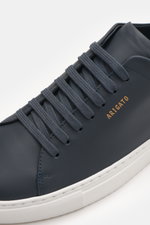 Close-up angled view of Axel Arigato Sneaker 'Clean 90' navy, featuring edles Glattleder, Veloursleder detail, runde Vorderkappe, sieben-Loch-Schnürung, goldfarbene Label-Prägung, gepolsterter Schaftrand, Innenfutter aus Leder, and flexible Gummisohle, id