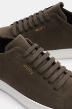 Close-up image of the Axel Arigato Sneaker 'Clean 90' graubraun photographed from a side angle, showing the minimalist grey-brown suede upper with round toe, seven-eyelet lacing, gold label embossing, padded collar, leather lining, and flexible white rubb