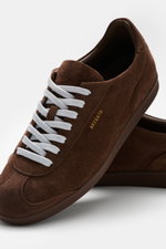 Close-up front-side view of Axel Arigato Sneaker 'Zane' braun in soft brown suede with white laces and gold branding, showing padded collar and rubber sole. <div class="qMYqUG_convSearchResultHighlightRoot">
<div class="" data-turn-id-container="request-W