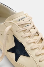 Golden Goose Sneaker "Super-Star Classic" creme/navy, Nahaufnahme von vorne schräg oben, Vintage-Finish, Nappaleder, navy Stern, Used-Optik, Sieben-Loch-Schnürung, gepolsterter Schaftrand.