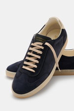 Brunello Cucinelli Sneaker navy aus geschmeidigem Veloursleder, retroeske Silhouette, beige Schnürung, Flügelkappe, Glattlederlasche, Naturgummisohle, seitliche Nahaufnahme.