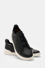 Zegna Slip-on Sneaker 'Triple Stitch' navy shown from a front side angle, made of grained leather with round toe cap, crisscrossed elastic bands, high padded collar, pull tab, embossed tongue, leather lining, and flexible rubber sole.