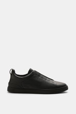 Zegna Slip-on Sneaker 'Triple Stitch' black shown in side profile, made of grained leather with crossed elastic bands, round toe, padded collar, pull tab, ZEGNA embossed tongue, leather lining, and flexible rubber sole. Inspired by ZEGNA's iconic stitchin