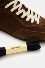 Close-up side view of the Axel Arigato Sneaker 'Daze Runner' dark brown in supple suede leather with cream laces and tonal overlays, showcasing the rounded toe cap, seven-eyelet lacing, padded collar, and flexible rubber sole. Minimalism in motion: The 'D