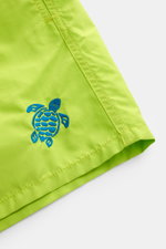 Vilebrequin Swim shorts 'Moka' neon green/teal, close-up angled view of fabric showing blue turtle stitching, high-quality microfibre with elastic waistband, pockets, drainage eyelets, and mesh lining for comfort and practicality.