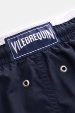 Nahaufnahme der elastischen Taille der Vilebrequin Badeshorts 'Moka' navy aus hochwertiger Microfaser mit weißem Bund, Metall-Entwässerungsösen und VILEBREQUIN-Weblabel, fotografiert von oben.
