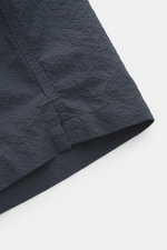 Close-up angled view of the hem of 04651/ A trip in a bag Swim shorts 'Mono Seersucker' navy, showing textured seersucker fabric.

<p>Perfect for your next summer holiday: With their design in seersucker look, these swim shorts by 04651/ A TRIP IN A BAG a