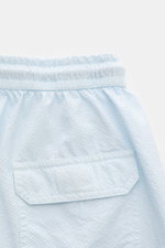 Close-up rear view of 04651/ A trip in a bag Swim shorts 'Mono Seersucker' pastel blue showing elastic waistband, seersucker texture, and back pocket with flap.

<p>Perfect for your next summer holiday: With their design in seersucker look, these swim sho