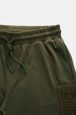 Nahaufnahme der Ché Sweat-Shorts "Inigo" dark olive von oben, zeigt weichen Baumwollstoff, regulierbaren Bund, Tunnelzug, Seitentaschen und Häkel-Tasche.