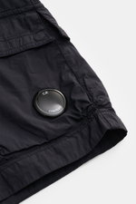 Nahaufnahme der C.P. Company Cargo-Bermudas navy von oben schräg, zeigt Cargo-Tasche, weiche Baumwoll-Microfaser-Mischung, Linsendetail.