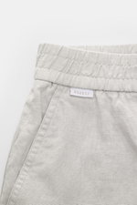 Nahaufnahme der 04651/ A trip in a bag Leinenshorts hellgrau von vorne oben, luftiges Leinengewebe, elastischer Bund, französische Taschen, kleines Weblabel am Bund.