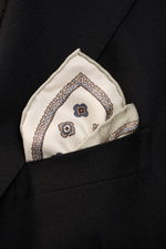 Brunello Cucinelli Silk pocket square sage/sand patterned folded in a black blazer pocket, close-up from a front angle. Noble accent: The silk pocket square by BRUNELLO CUCINELLI features a subtle medallion pattern that adds a discreet highlight and compl