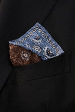Close-up angled view of Brunello Cucinelli Silk Pocket Square grey blue/brown patterned in a black blazer pocket, showcasing pure silk, smooth feel, subtle medallion pattern, rolled edges, made in Italy, approx. 35x35 cm.

<p>Noble accent: The silk pocket